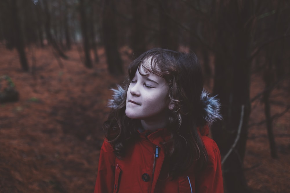 girl wearing red coat standing near trees