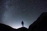 silhouette of man standing on hill during starry night