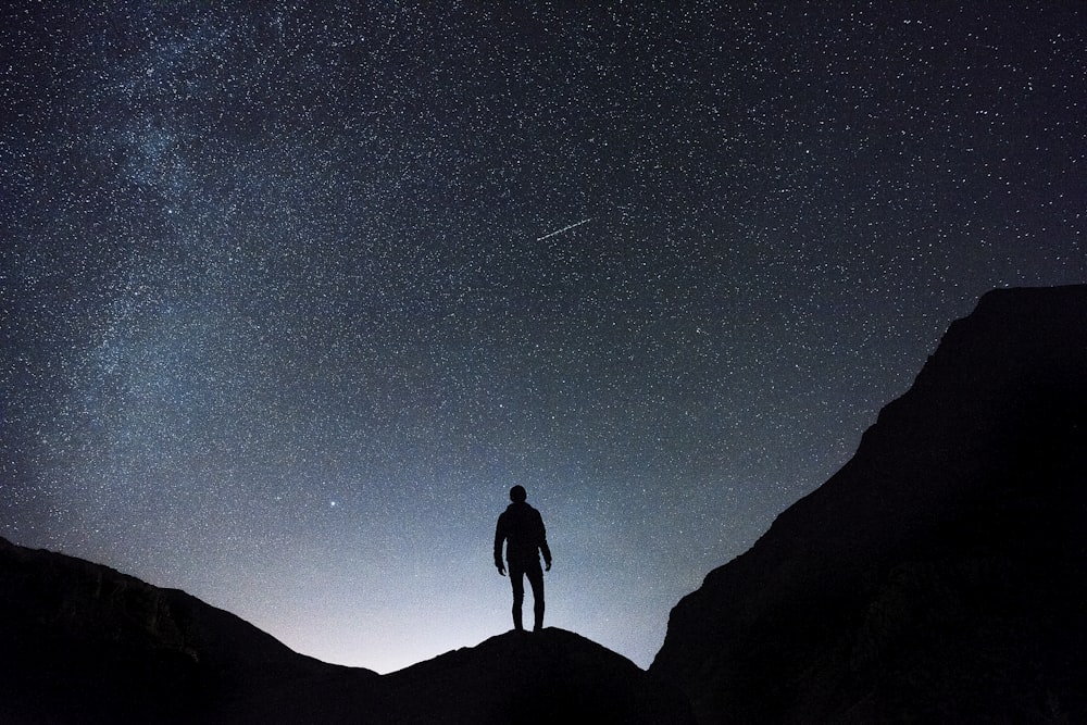 Silhouette eines Mannes, der in der sternenklaren Nacht auf einem Hügel steht