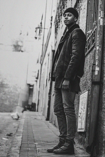 Black and white photo of a city alley with a person wearing a Junkwear hoodie, embodying street culture.