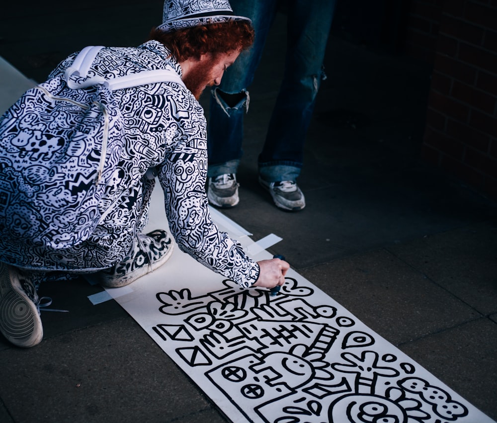 man drawing on white paper while kneeling at daytime