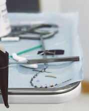 A close-up view of a medical tray with various dental tools, including a dental drill, orthodontic braces, and a small green dental brush on a blue sterile cloth.
