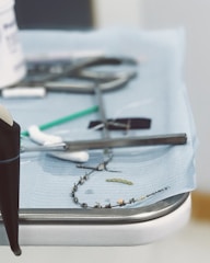 A close-up view of a medical tray with various dental tools, including a dental drill, orthodontic braces, and a small green dental brush on a blue sterile cloth.