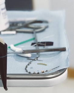 A close-up view of a medical tray with various dental tools, including a dental drill, orthodontic braces, and a small green dental brush on a blue sterile cloth.
