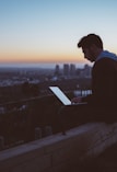 man sitting on concrete brick with opened laptop on his lap