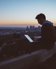 man sitting on concrete brick with opened laptop on his lap