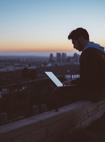 man sitting on concrete brick with opened laptop on his lap