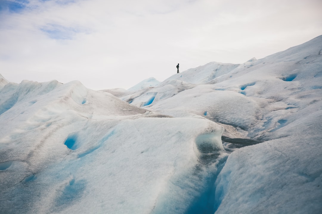 person standing on top of hill under white cloud blue skies, Tour guide exploring trekking conditions on Perito Moreno g