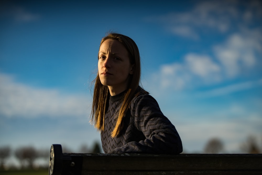 woman in gray sweater leaning on wooden bench backrest