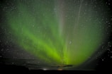 A night sky filled with stars and a faint electric green aurora shimmering above.