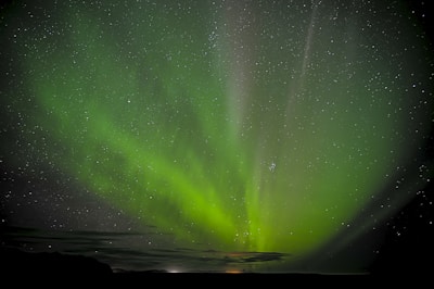 A night sky filled with stars and a faint electric green aurora shimmering above.