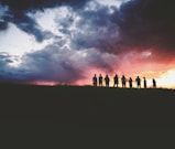 silhouette of nine persons standing on the hill