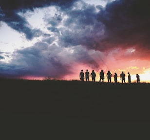 silhouette of nine persons standing on the hill