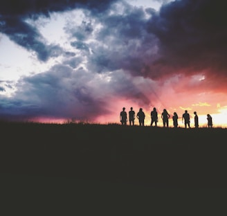 silhouette of nine persons standing on the hill