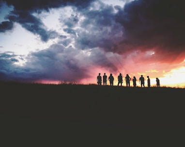 silhouette of nine persons standing on the hill
