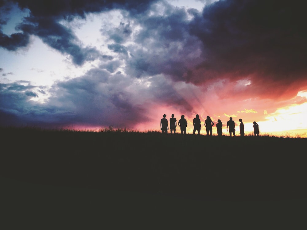 Silhouette von neun Personen, die auf dem Hügel stehen