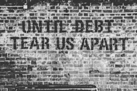 Large text is stenciled on a brick wall with the phrase 'UNTIL DEBT TEAR US APART'. The wall is made of dark bricks and the image is in black and white, creating a gritty, urban feel.