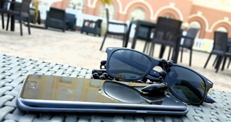 Close-up of sleek, ultra-lightweight sunglasses resting on a wooden table outdoors with sunlight filtering through leaves.