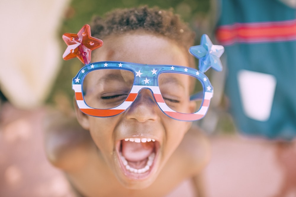 niño con gafas impresas con la bandera estadounidense que saca la boca abierta