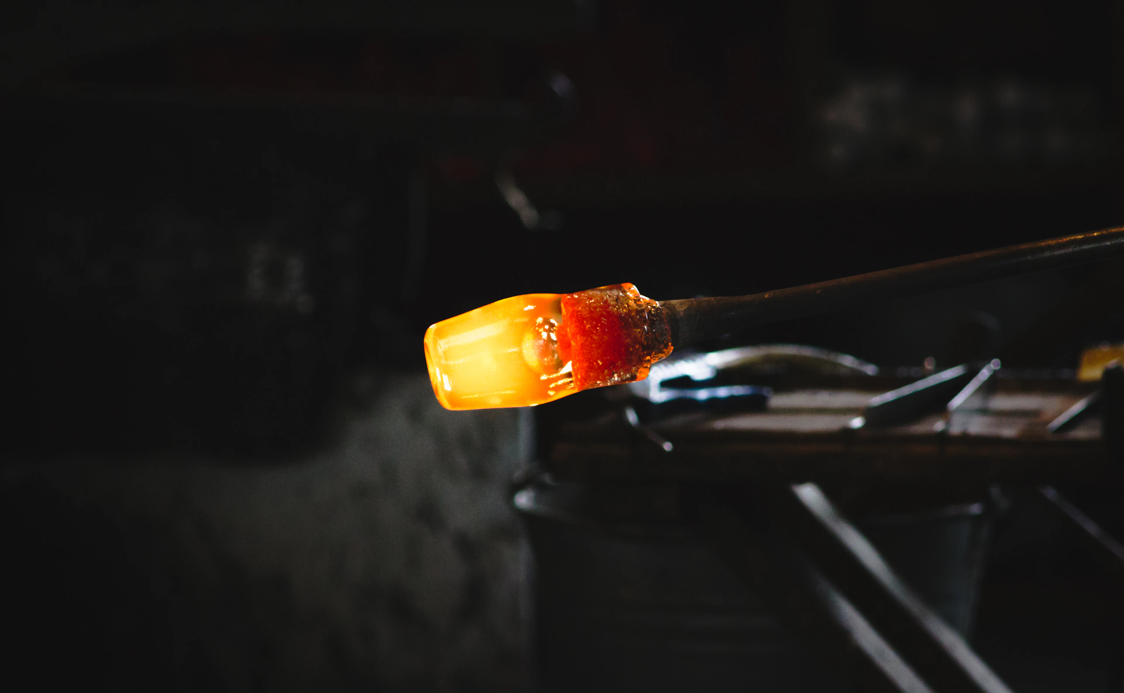 A glowing lump of molten glass on a rod, mid-shape at a glassblower's workshop.