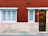 A red brick building facade featuring two windows with white frames and blue security bars on the left, and a brown wooden door with a mailbox slot on the right. The wall also has a small decorative plant above the door number sign.