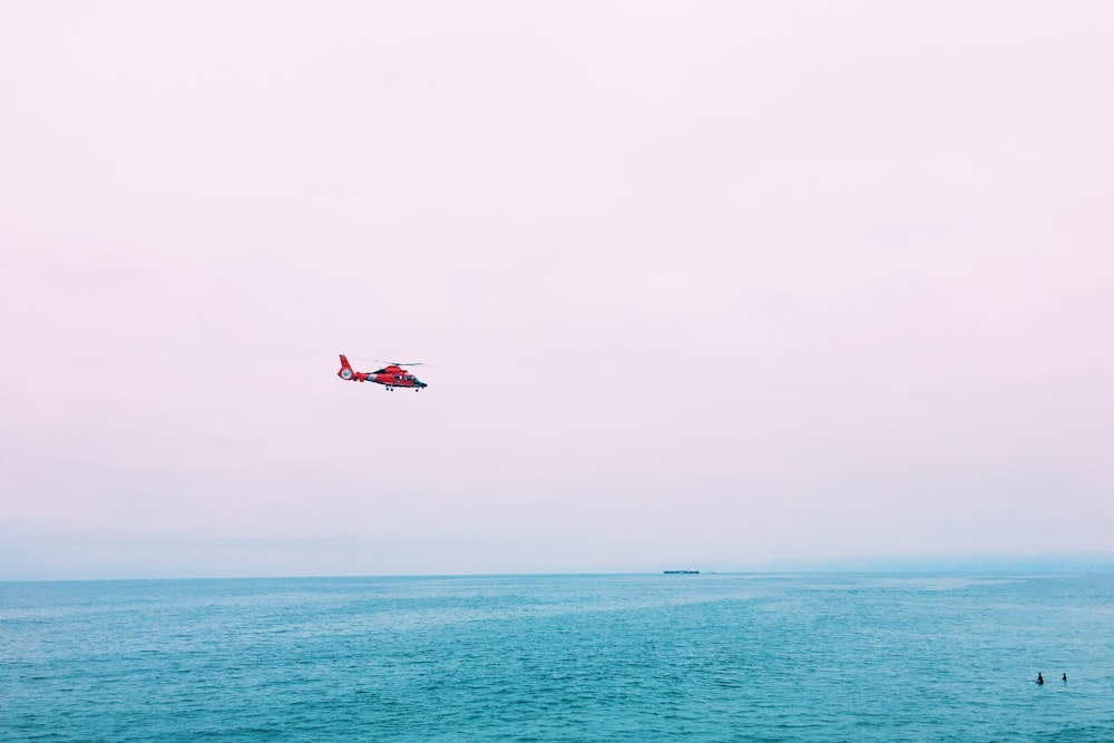 red plane on mid air above sea