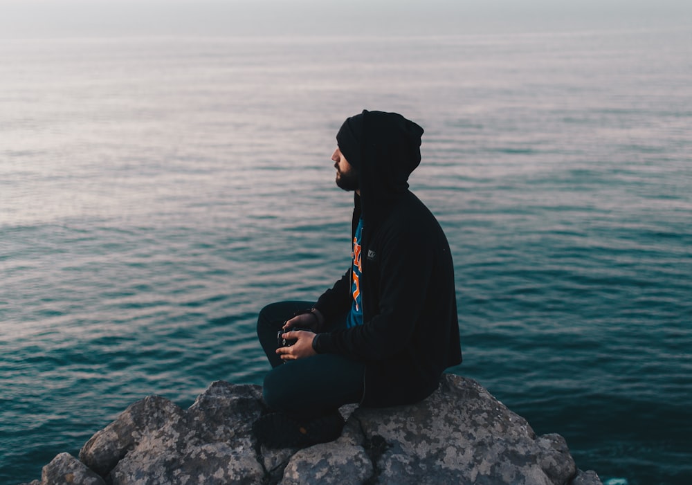 homem sentado na rocha perto da água do oceano