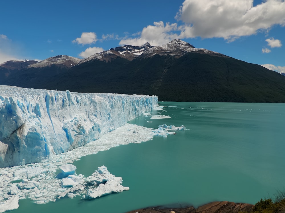 ice berg near mountain under cloudy sky