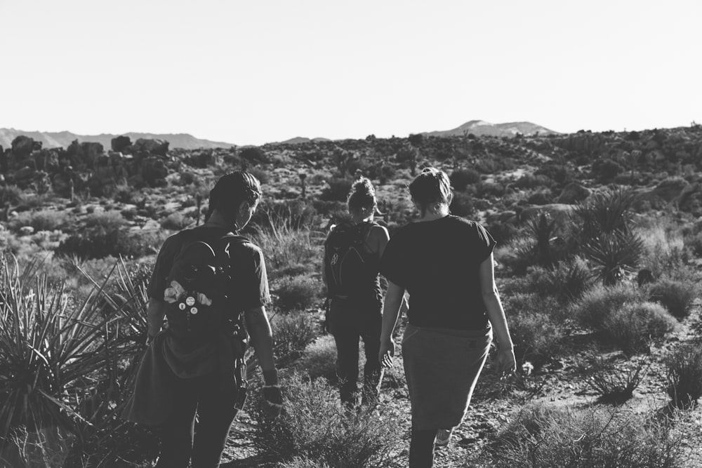 grayscale photography of three women trekking on empty field