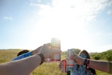 Friends laughing and clinking pop stream cans at a sunny outdoor picnic with vibrant decorations.