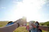 A playful moment of friends balancing beer glasses on their heads at a sunny outdoor gathering.