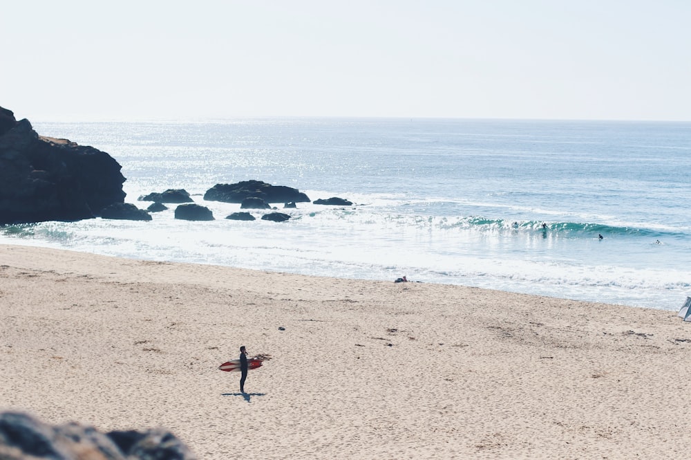 man holding red surfboard on beach