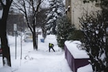 Staff member clearing snow from a walkway with a shovel in a quiet neighborhood.