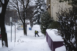 Action shot of a person in winter gear pushing snow with a shovel on a residential sidewalk.