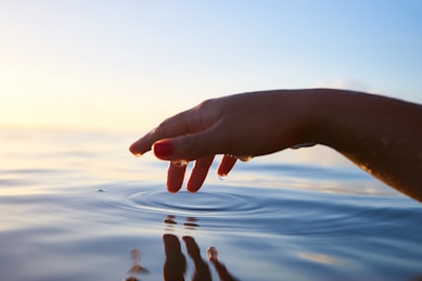 person about to touch the calm water with hand with serene soft sun in background