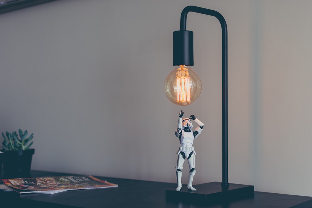 A figurine of a stormtrooper under a desk lamp with an incandescent light bulb