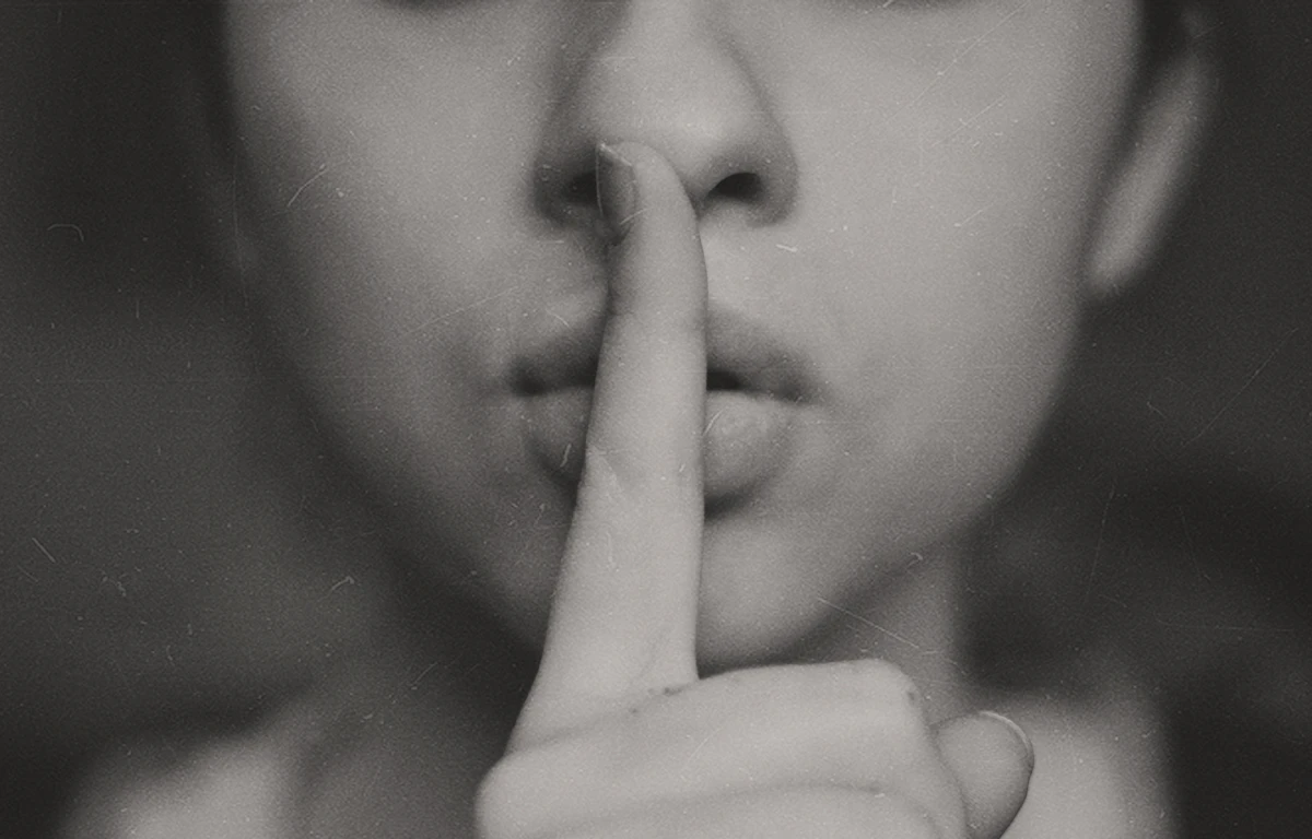 Black and white close-up of a woman with her finger gently to her lips, representing the quiet and unspoken weight of always appearing okay