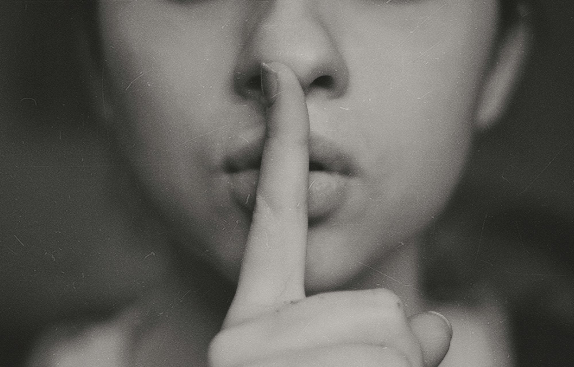 a close-up of a person putting their finger over their lips in a "shush" gesture 