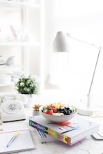 A clean, modern workspace with nutrition books and fresh fruits on a white table.