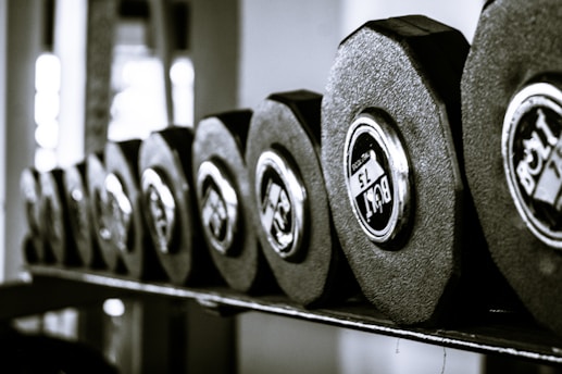 A row of hexagonal dumbbells neatly arranged on a rack, with the weight labels visible on their ends. The image is captured with a shallow depth of field, highlighting the texture and metallic shine of the weights.