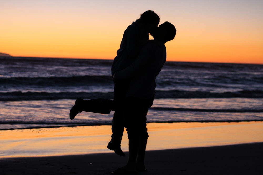 Foto da silhueta do casal se beijando perto do mar durante a hora dourada