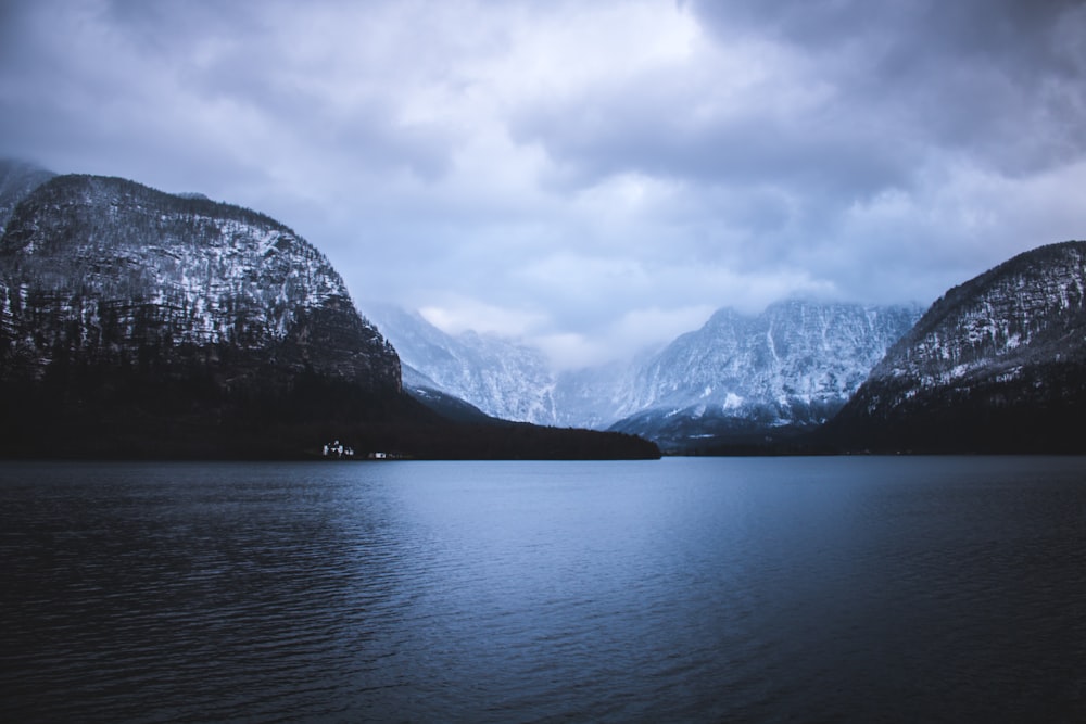 Landschaftsfotografie von Bergen in der Nähe eines Gewässers unter bewölktem Himmel