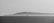A stark black and white photograph capturing a solitary offshore oil rig against the backdrop of a distant, misty island across the water. The calm sea reflects the overcast sky, creating a serene yet somewhat isolated atmosphere.