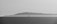 A stark black and white photograph capturing a solitary offshore oil rig against the backdrop of a distant, misty island across the water. The calm sea reflects the overcast sky, creating a serene yet somewhat isolated atmosphere.