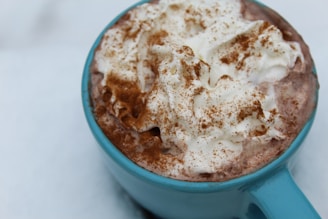 A close-up view of a blue mug filled with hot chocolate, topped with a generous amount of whipped cream and sprinkled with cinnamon.