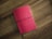 A red notebook with a textured cover lies flat on a wooden surface. It is secured with a black elastic band that wraps around its middle.