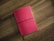 A red notebook with a textured cover lies flat on a wooden surface. It is secured with a black elastic band that wraps around its middle.