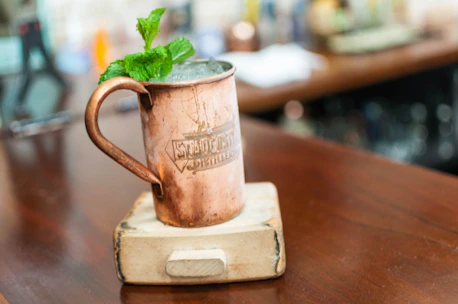 Set of polished pure copper mugs filled with iced beverages, surrounded by fresh herbs.