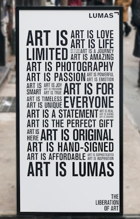 A black and white poster with various motivational phrases about art arranged in different fonts and sizes. Words include 'Art is love', 'Art is life', 'Art is a journey', among others. The poster has a minimalist design and is placed outside on what appears to be a city street.