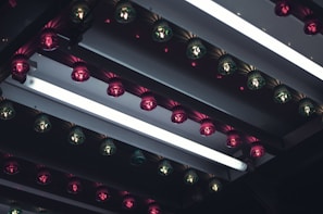 A series of light bulbs arranged in rows, featuring alternating pink and green colors, mounted on a reflective metallic surface with strips of LED fluorescent lighting. The setup creates an industrial and somewhat nostalgic ambiance.